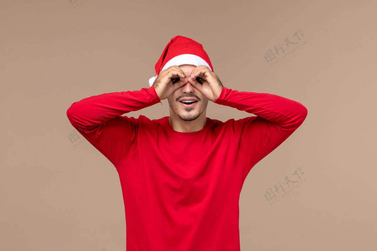 快乐前视图年轻男性透过手指看棕色背景圣诞假期的情绪男性视图看