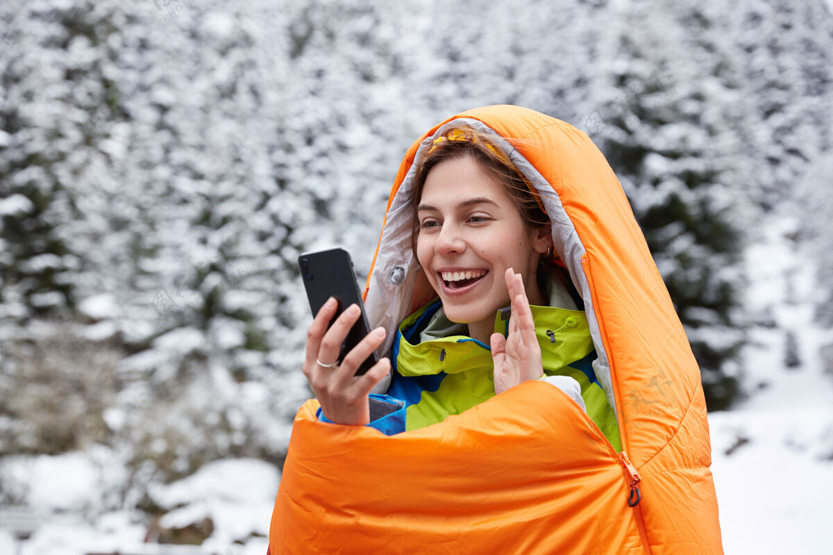 远足快乐的女人在手机的镜头前高兴地挥手 在雪山上做视频通话自然极限装置