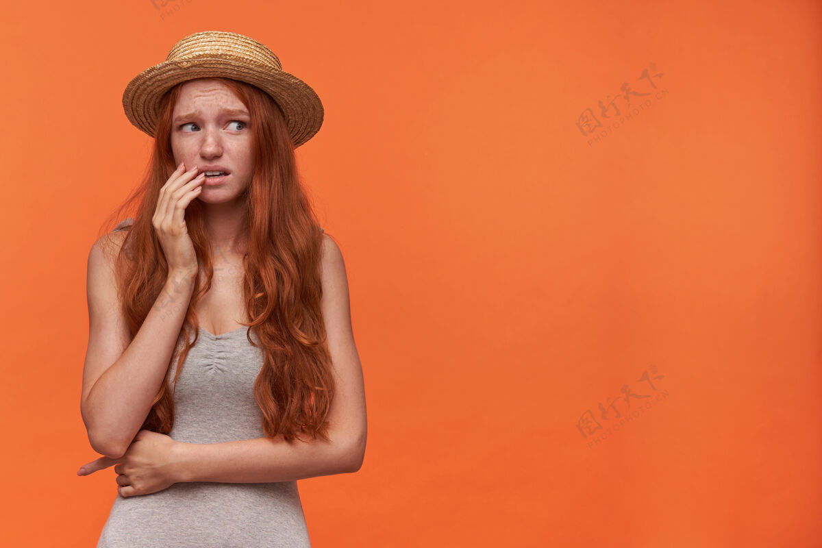 肖像吓坏了年轻的狐狸精长发女人站在橙色的背景下 手放在脸上 惊恐地皱着眉头 穿着休闲服女士情绪帽子