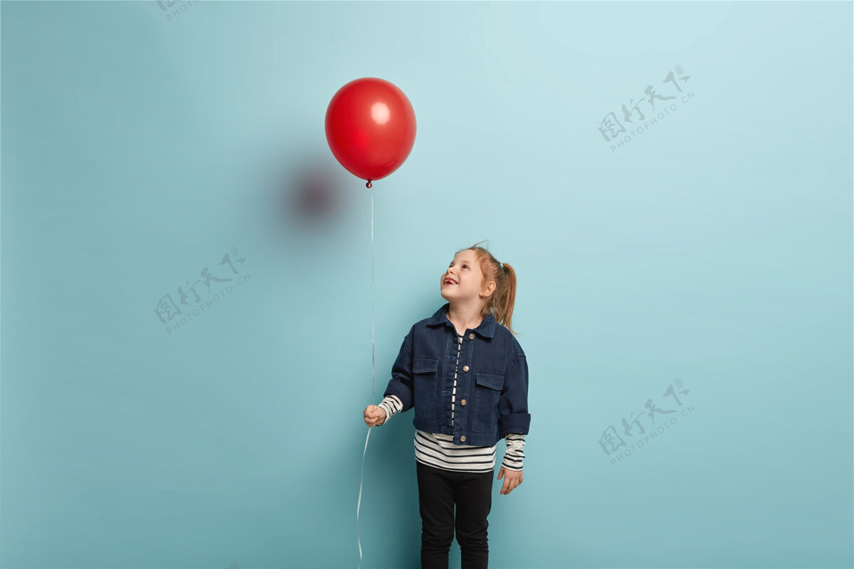 条纹生日派对和童年概念姜黄色头发的快乐小孩横拍 在红色气球上快乐地向上看 穿着时髦的衣服 站在蓝色的墙上小高兴夹克