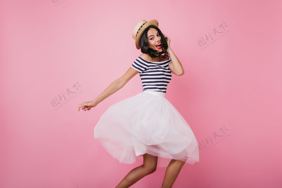年轻滑稽的拉丁女人戴着草帽表达幸福和舞蹈情绪化的女模特穿着白色裙子摆姿势裙子现代人