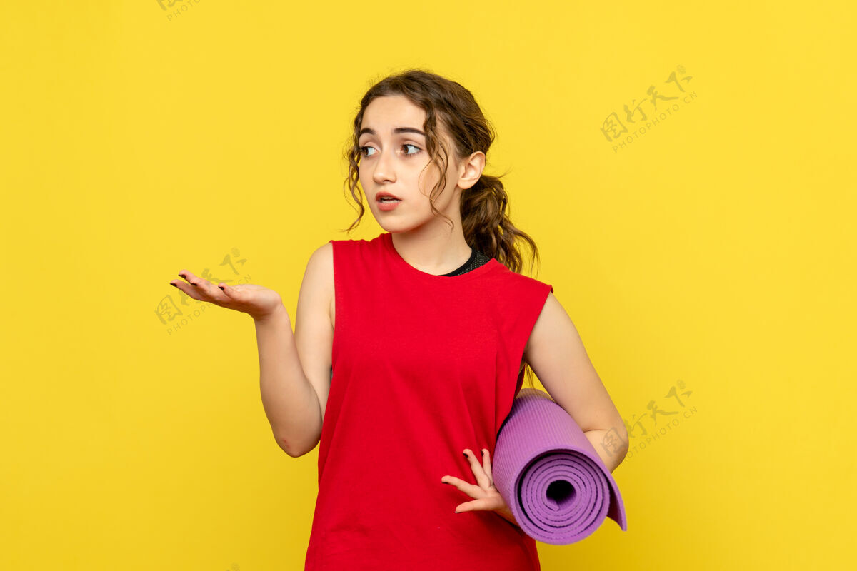 人浅黄色墙上拿着紫色地毯的年轻女子的正视图紫色黄色漂亮