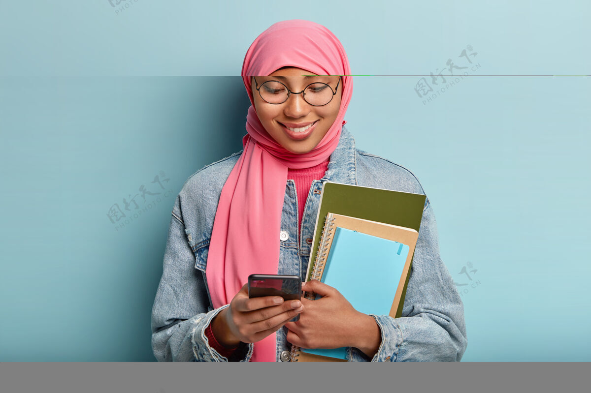 手机可爱的微笑女性裹着粉色面纱 在大学学习持有信息青少年