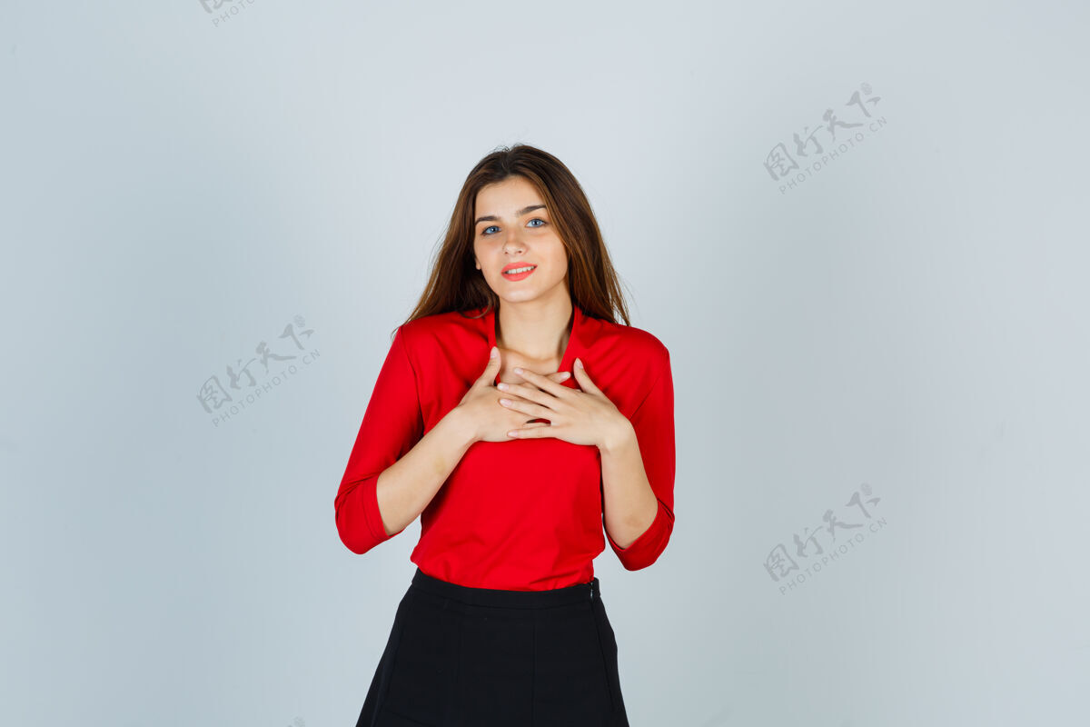 手一个穿着红衬衫 黑裙子的年轻女人 手放在胸前 看起来很快乐快乐人美丽