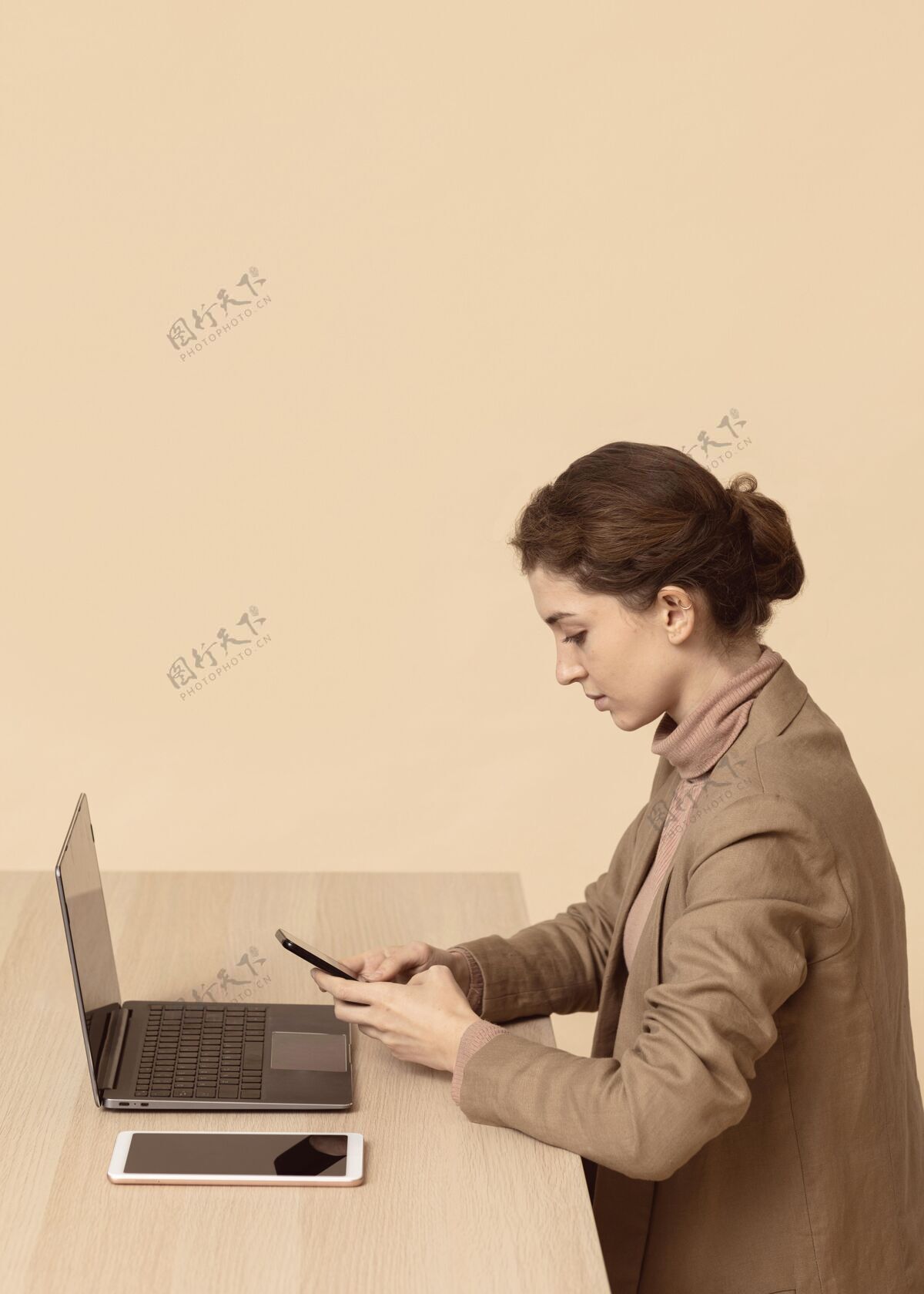 设备坐在笔记本电脑旁使用智能手机的女人模特数码姿势