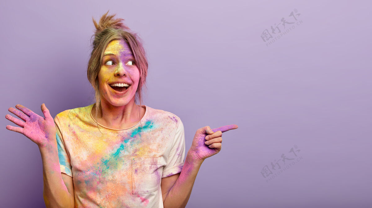 光明快乐快乐的女人的肖像有肮脏的脸和彩色染料的衣服 庆祝印度的胡里节 展示紫色墙壁上的自由空间颜色的节日促销概念个性指向白种人