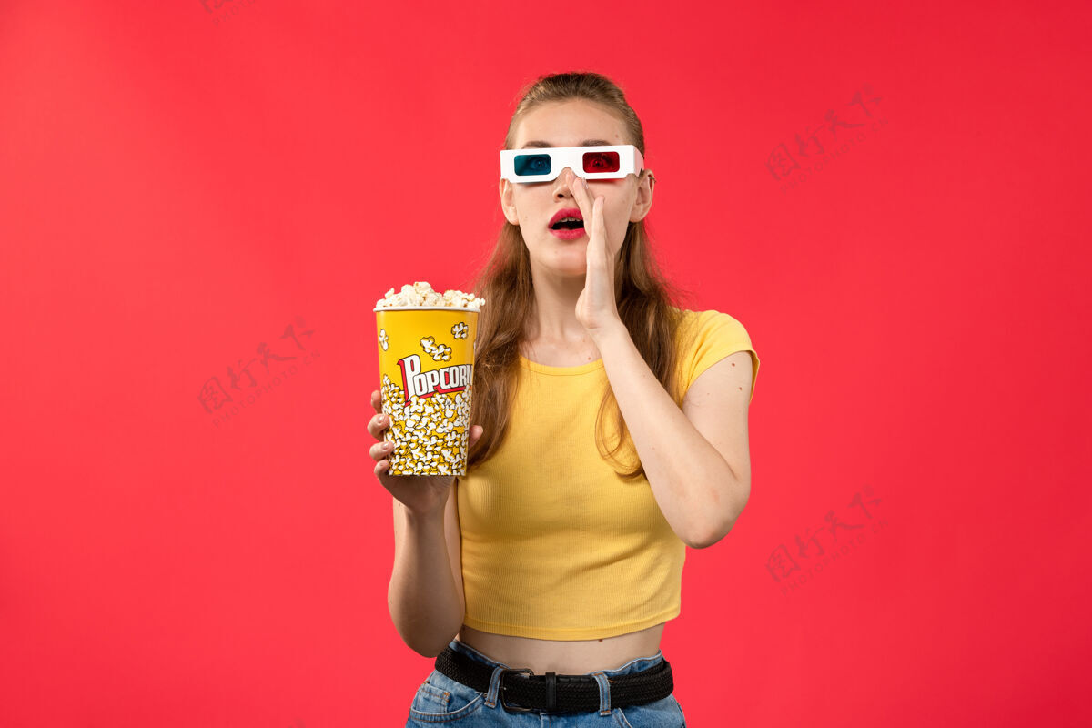 爆米花正面图年轻女性在电影院拿着爆米花在红墙电影院的d太阳镜电影院小吃女性趣味电影小吃电影女性