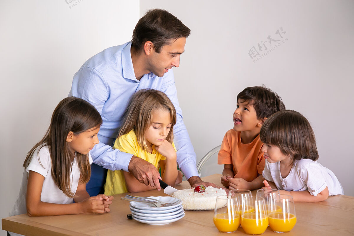童年白种人的父亲为孩子们切美味的蛋糕可爱的小朋友围着桌子 一起庆祝生日 聊天和等待甜点童年 庆祝和节日的概念小甜点可爱