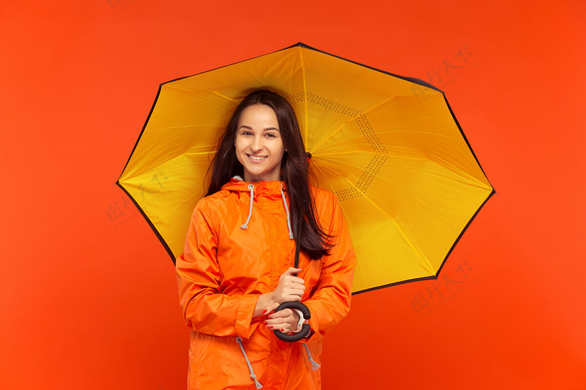 站立一个快乐的微笑着的小女孩穿着秋天的橘色夹克在摄影棚里摆姿势雨肖像成人