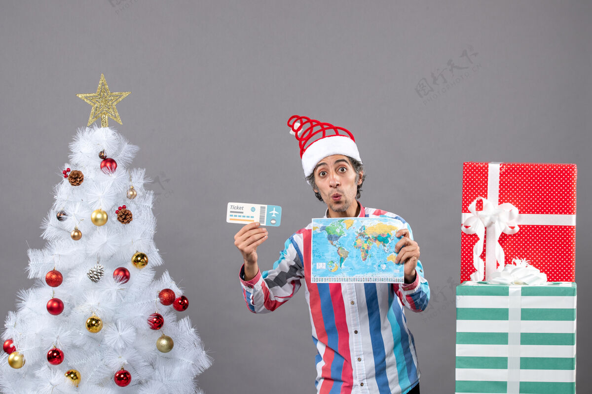 火炬前视图惊讶的男子与螺旋弹簧圣诞帽举行世界地图和旅行票快乐惊喜地图