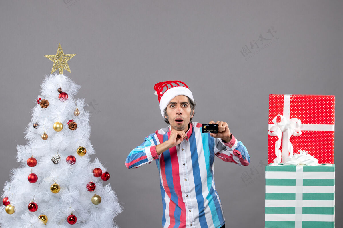 灰色前视图：一个站在圣诞树旁的男人把手放在下巴上专业人成人