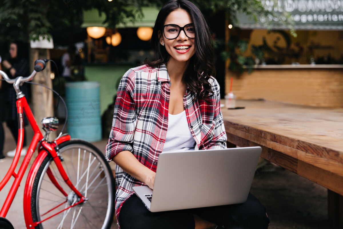 休闲笑容可掬的拉丁黑发女孩摆着自行车和笔记本电脑的姿势快乐时尚的女士拿着电脑坐在街上自行车户外城市