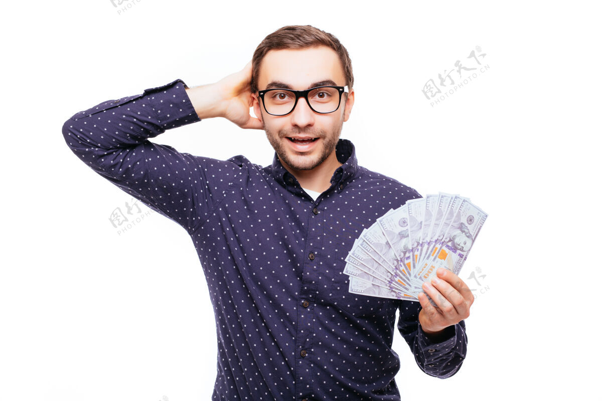 金钱一个激动得不知所措的男人拿着一堆钞票 看着隔着白墙的摄像机人经济货币
