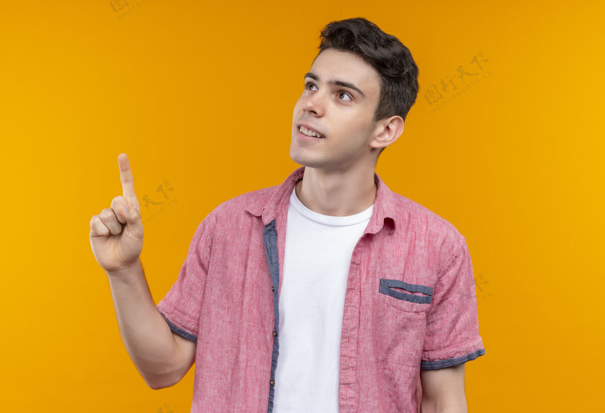 粉色微笑的白人年轻人穿着粉色衬衫指着孤立的橙色背景点向上小伙子