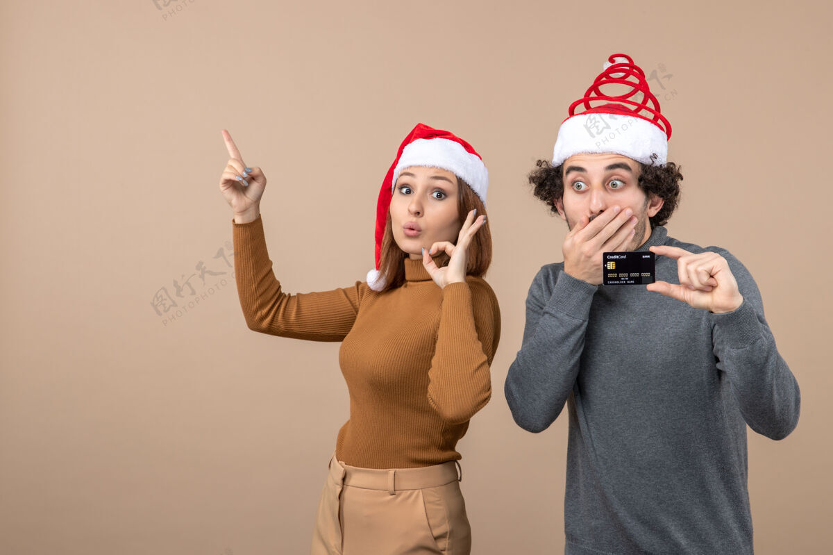 红色圣诞节心情激动酷情侣戴红色圣诞老人帽男人出示银行卡女人指着上面卡片指向圣诞节