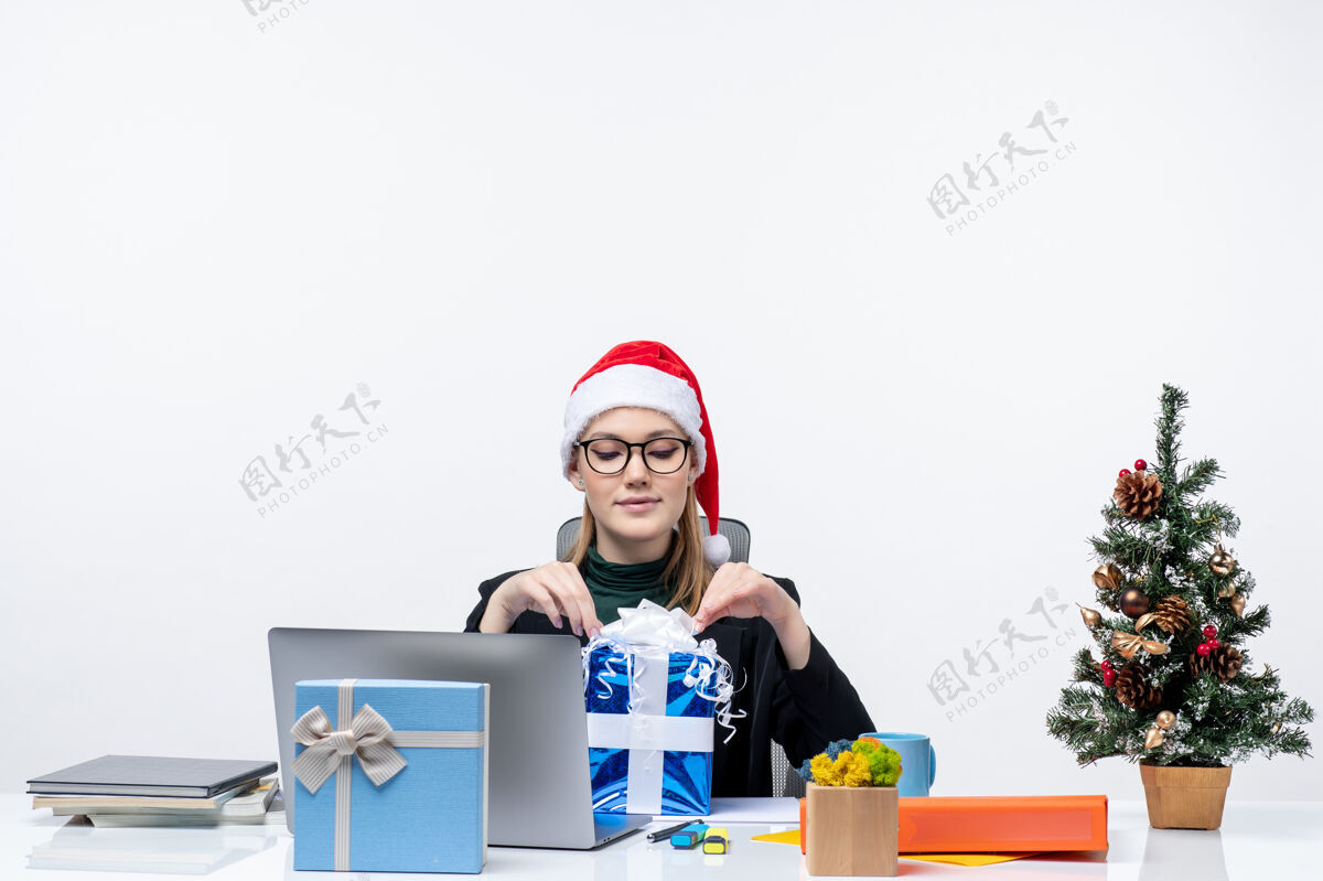 圣诞老人圣诞气氛与戴着圣诞老人帽子和眼镜的年轻女子坐在一张桌子旁打开白色背景的礼物帽子笔记本电脑桌子