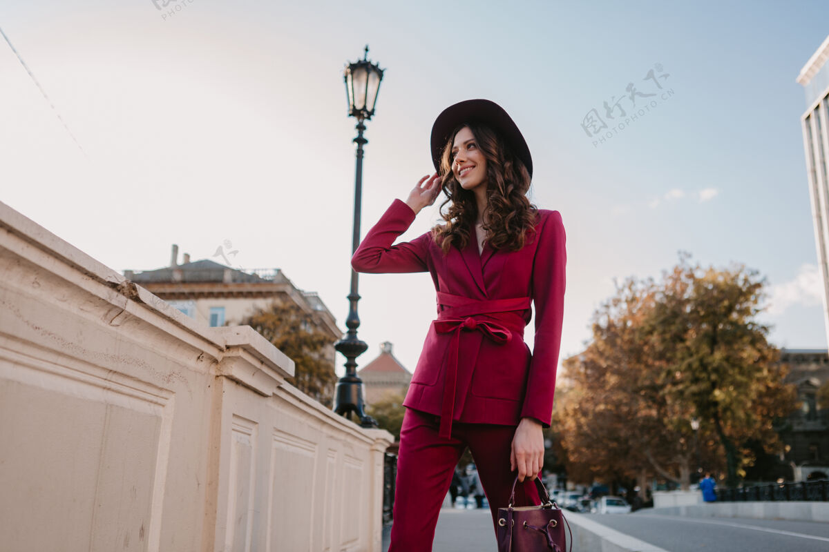 优雅穿着紫色西装的漂亮时髦女人走在城市街头 春夏秋冬时节时尚潮流戴着帽子 手拿钱包时尚女人套装