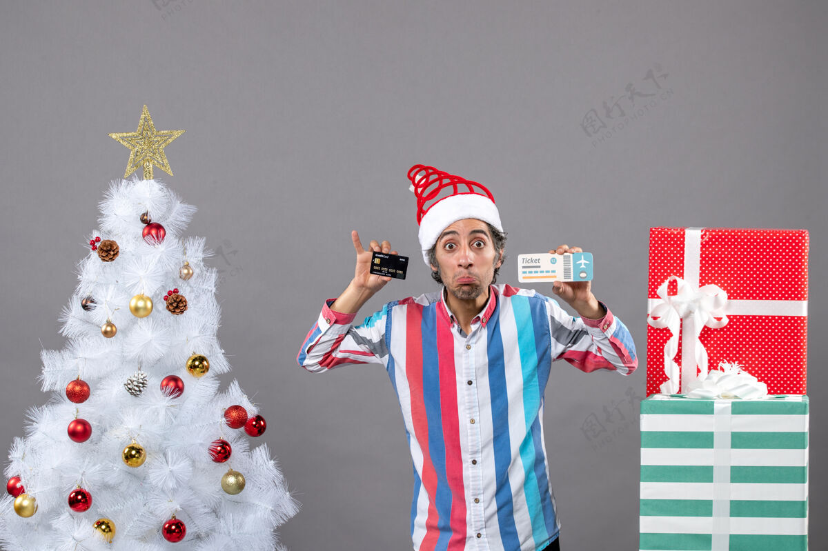 人前视图：一个眼睛敏锐的男人拿着卡片和旅行票 围着圣诞树和礼物人树男性