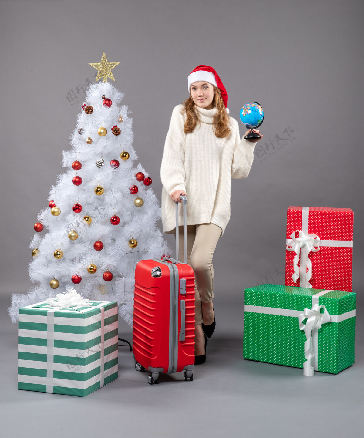 圣诞正面图金发女孩戴着圣诞帽拿着地球仪和红色手提箱假日快乐礼品盒