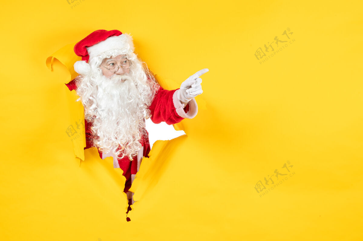 纸圣诞老人透过撕破的纸黄色墙壁看的正视图圣诞老人看圣诞