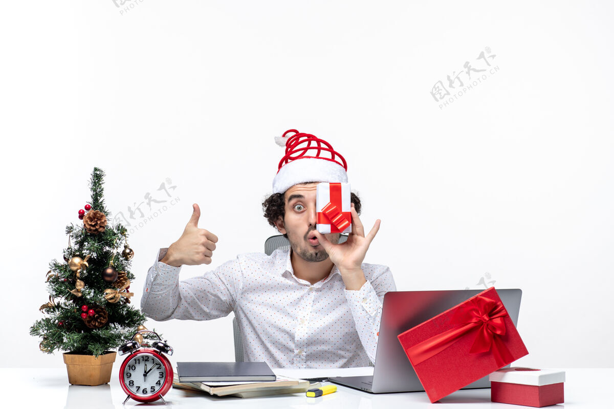 圣诞老人圣诞节心情与有趣的商人与圣诞老人的帽子提高他的礼物 他的脸 并作出完美的姿态在白色背景圣诞节手势圣诞老人