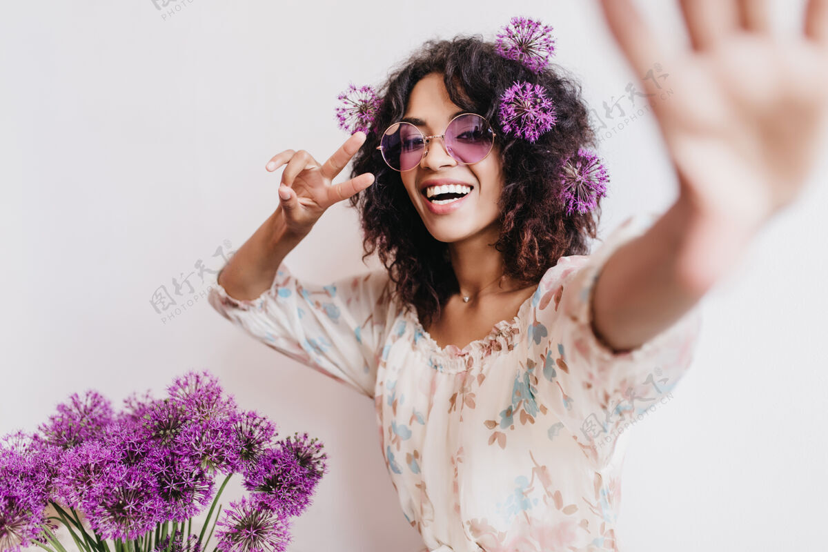 模特热情的非洲女孩穿着时尚的礼服与葱自拍壮观的黑人年轻女子在室内与紫花合影时玩得很开心开花室内植物