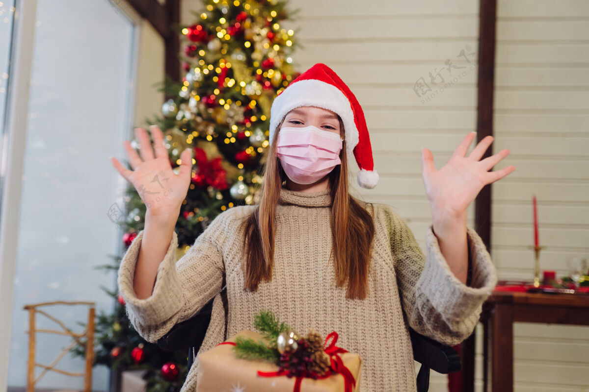 年轻女孩在新年前夜挥手圣诞树冠状病毒期间的圣诞节 概念圣诞老人松树冠状病毒
