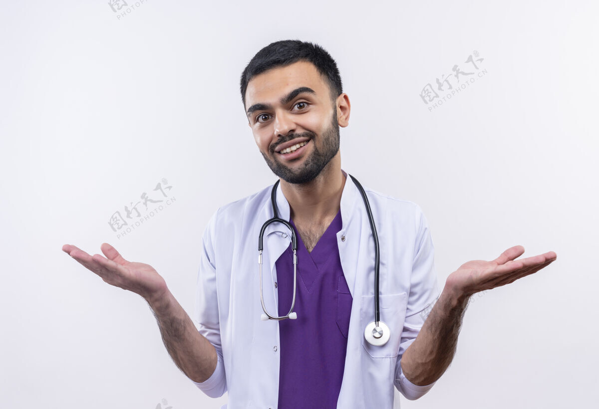 穿着微笑的年轻男医生穿着听诊器医用长袍 在孤立的白色背景上展开双手男性年轻医疗
