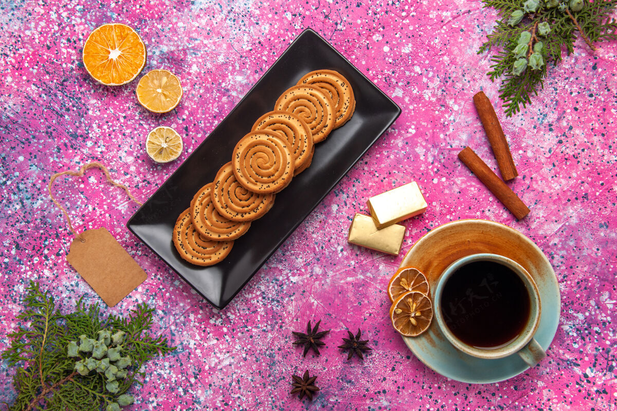 肉桂顶视图中的甜饼干与肉桂和茶在浅粉红色的表面黑色形式糖果美味热的