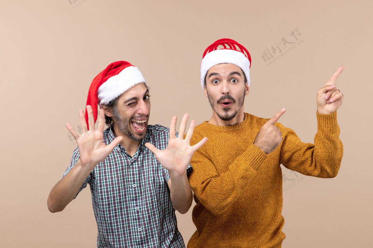 头饰正面图两个戴着圣诞帽的快乐男人一个在展示什么 另一个在孤立的背景上击掌帽子男人圣诞老人