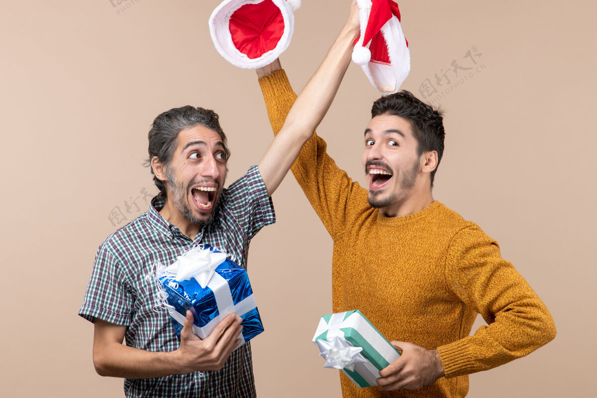 米色正面图：两个快乐的家伙拿着圣诞礼物 在米色孤立的背景下 两人互相摘下帽子成人快乐风景