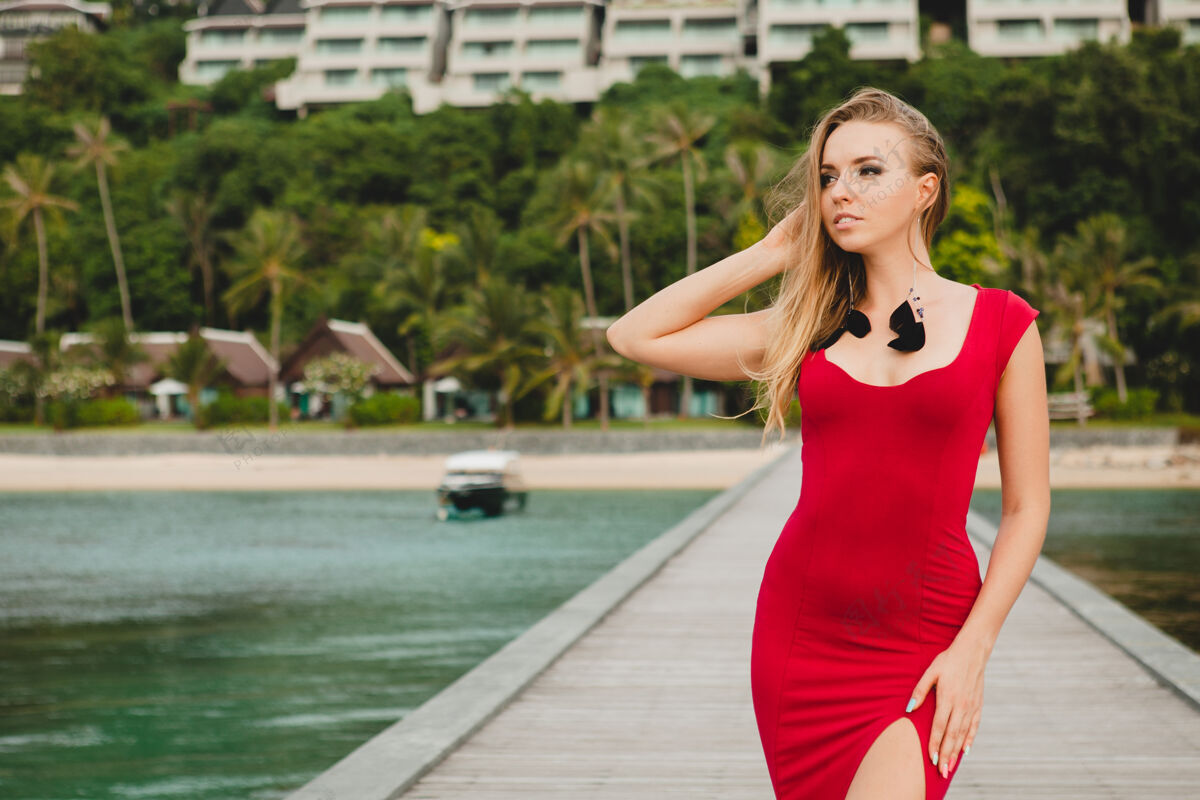 异国情调年轻漂亮迷人的女人独自站在豪华度假酒店的码头上 暑假 红色长裙 金色头发 性感服装 热带沙滩 诱惑 性感 微笑美腿身体人