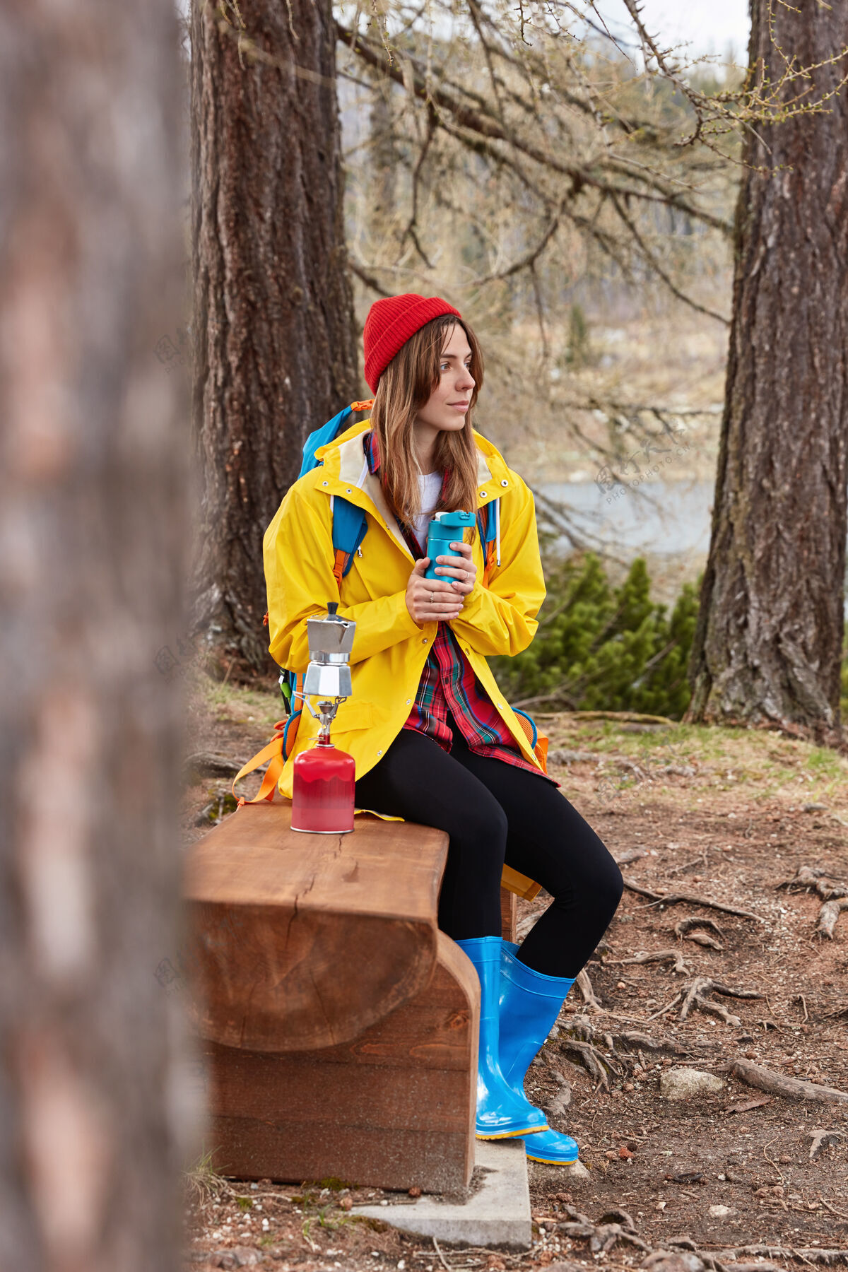 自然图为体贴的女游客在森林里的木凳上休息 用热水瓶喝茶 在野营的炉子上煮咖啡 戴着红帽子饮料茶紧身裤
