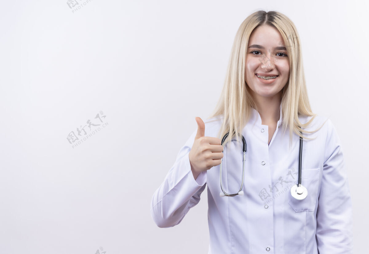 女孩微笑的医生年轻的金发女孩戴着听诊器和医用长袍在牙科支撑她的拇指上孤立的白色背景白人拇指听诊器