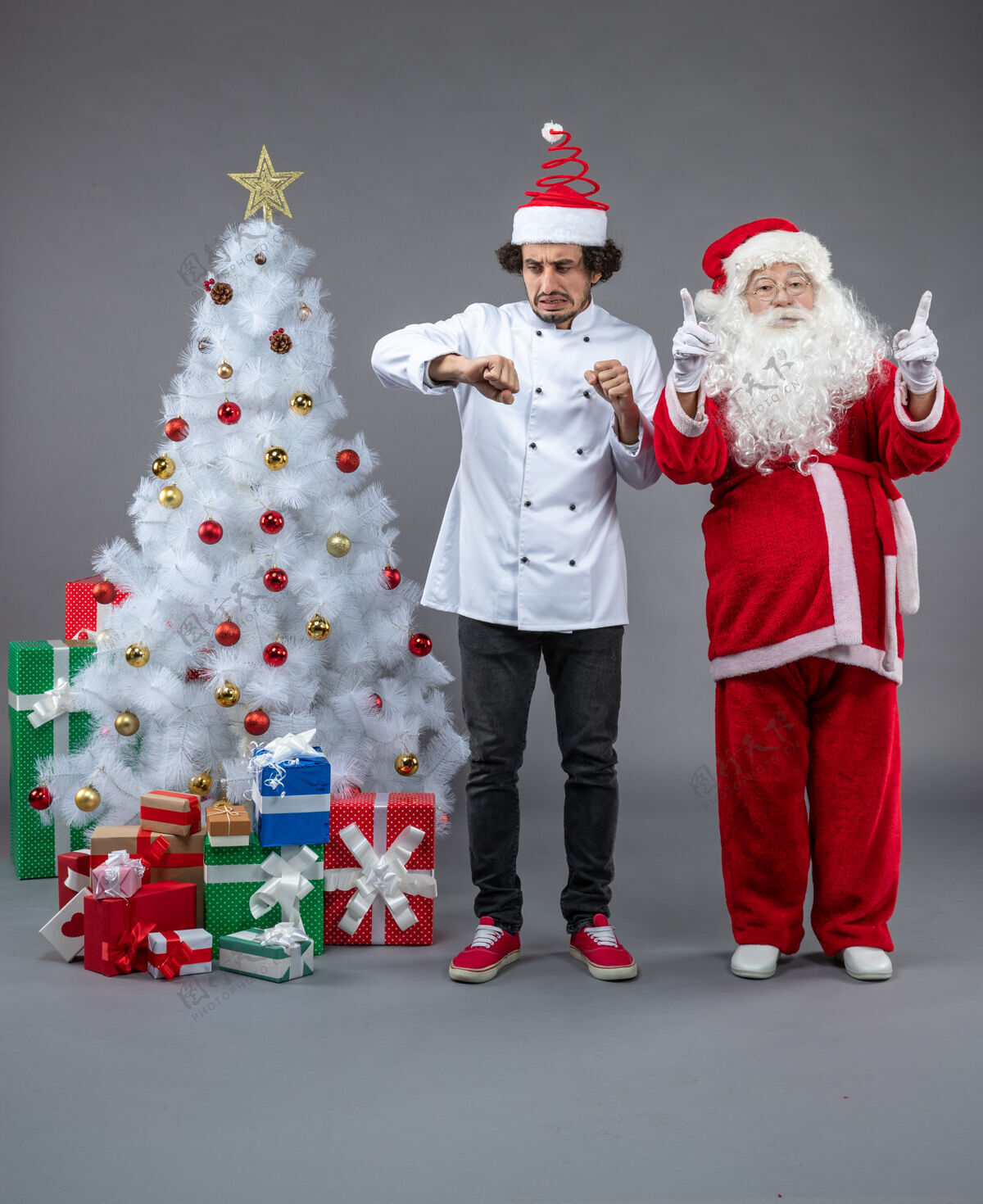 节日圣诞老人和男厨师在灰色墙上围着圣诞礼物的正视图厨师人圣诞老人