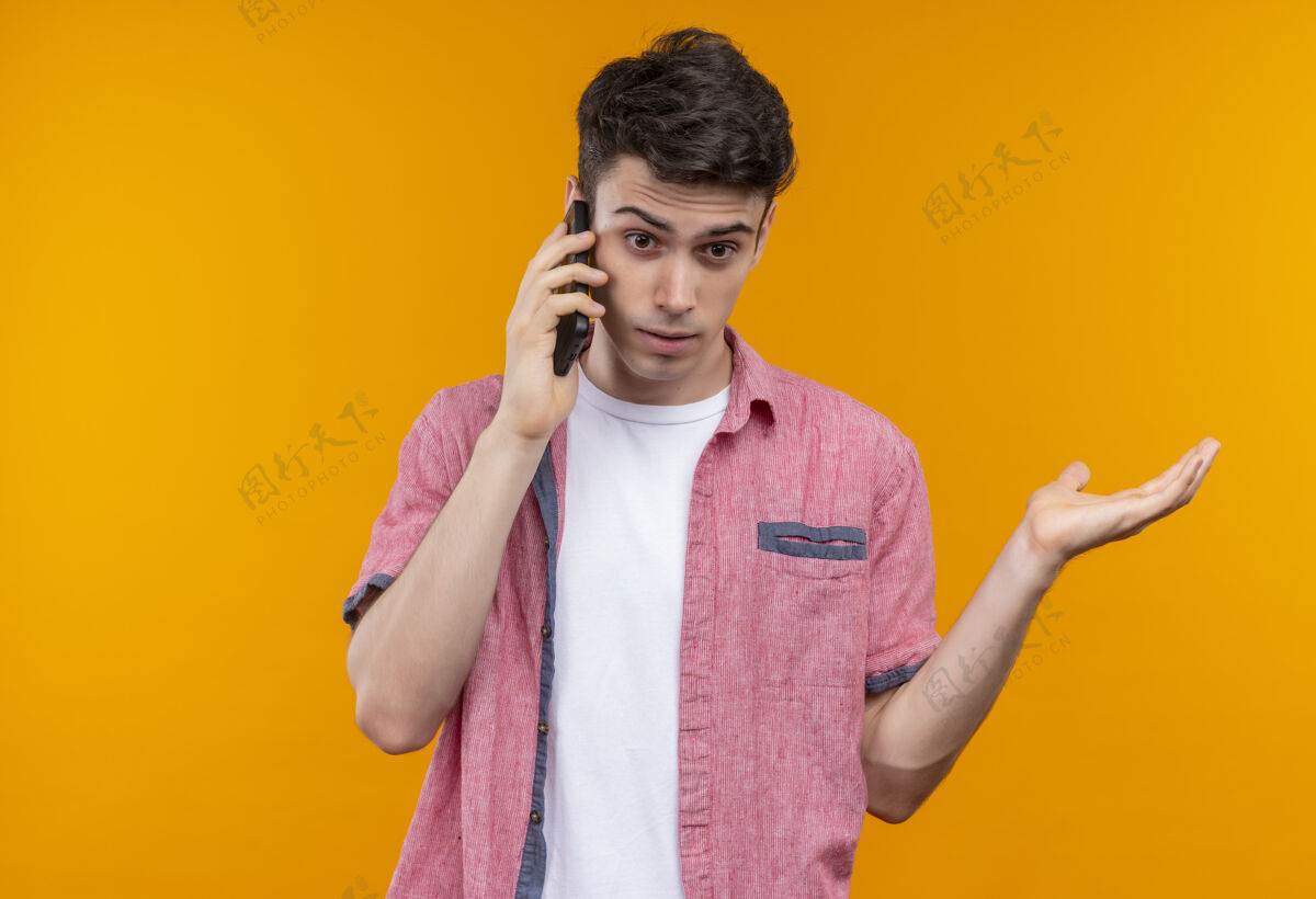 举起一个穿着粉色衬衫的白人年轻人在孤立的橙色背景下举手打电话惊讶说话戴着