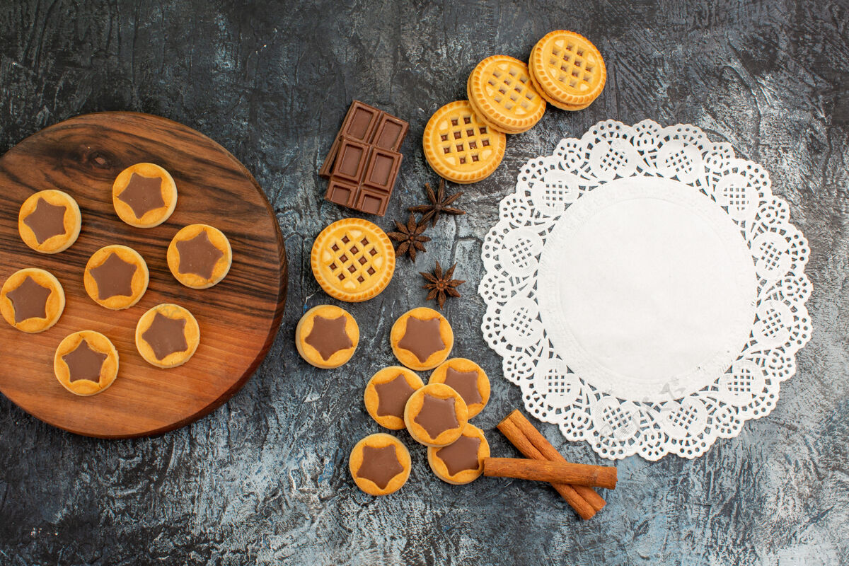 顶部木制盘子上的饼干和白色蕾丝的顶视图 灰色背景上有肉桂和巧克力白色拼盘灰色