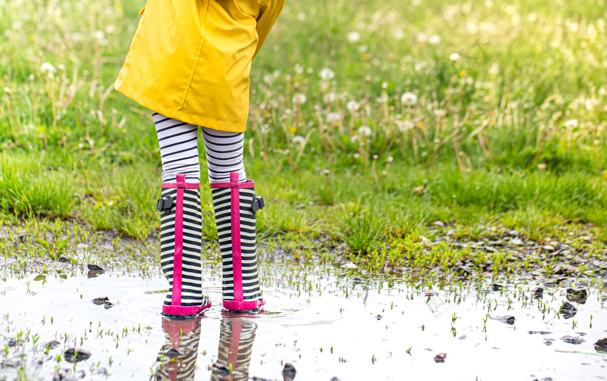橡胶穿着亮黄色雨衣和条纹胶靴的小孩雨衣童年水坑