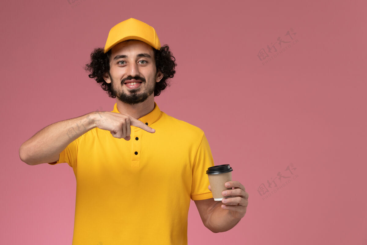快递正面图：身穿黄色制服 披风的男性快递员手持粉色墙上的送货咖啡杯工人男快递粉色