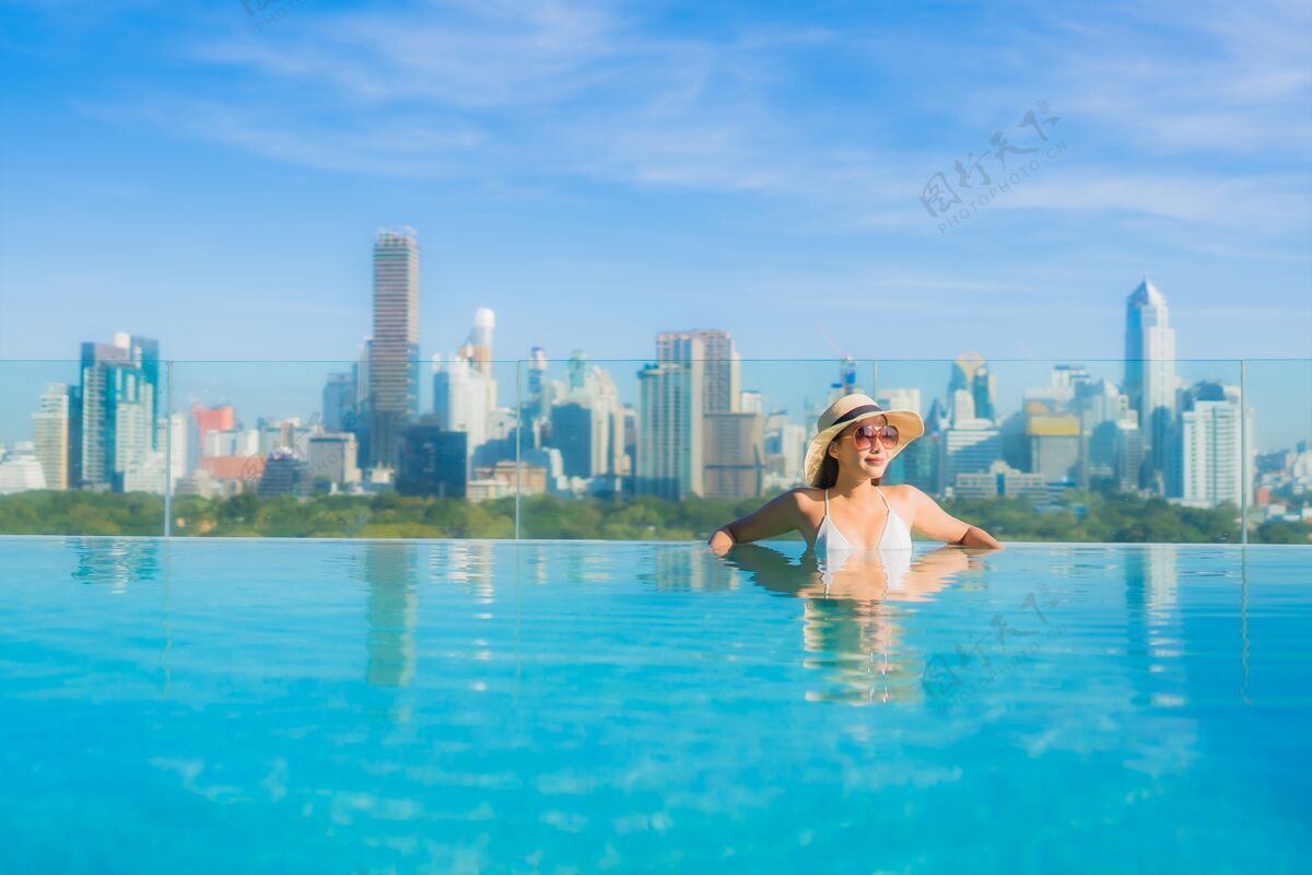 屋顶肖像美丽的亚洲年轻女子微笑放松休闲围绕室外游泳池与城市景观身体著名城市