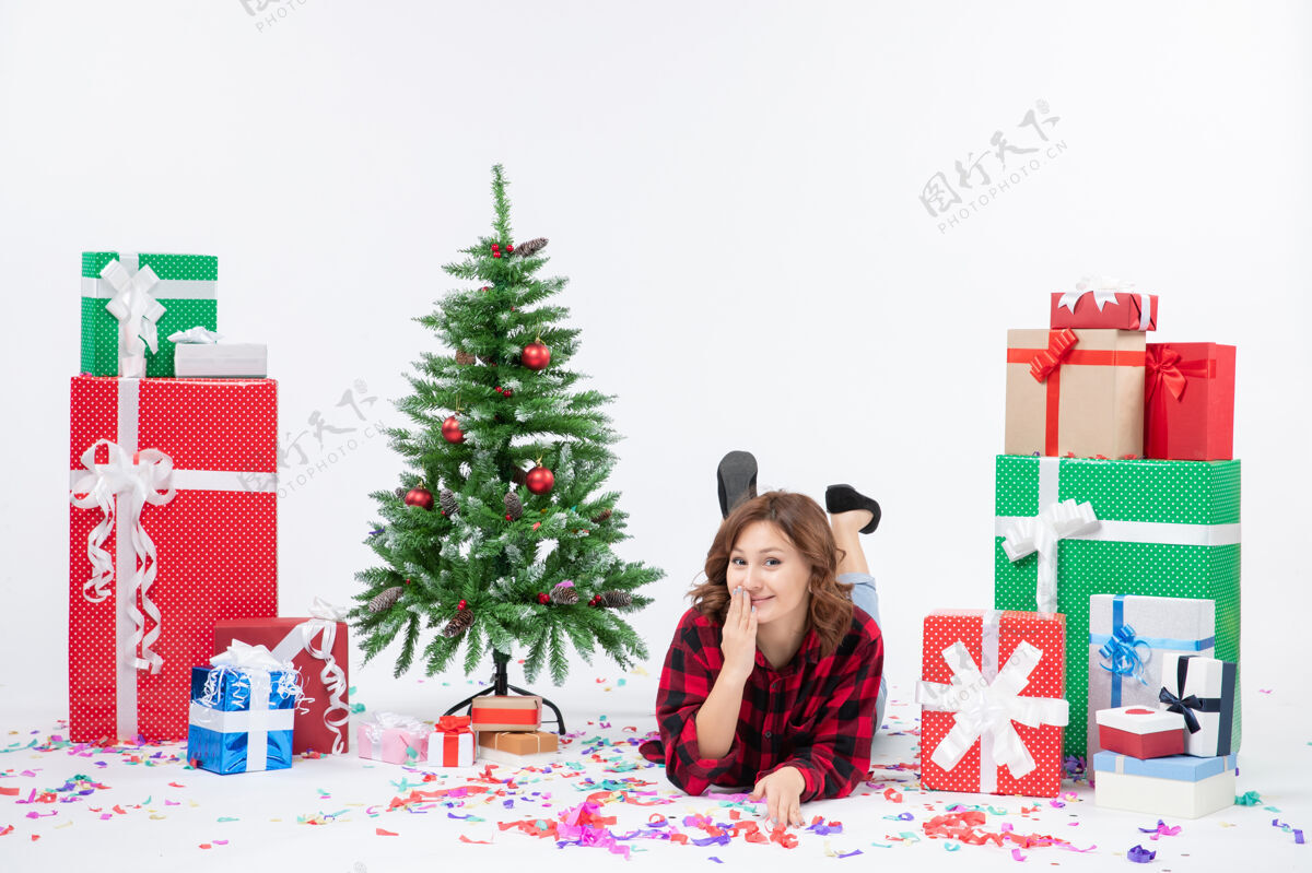 铺设正面图：年轻女性躺在白色背景上的圣诞礼物和圣诞树上 圣诞礼物的颜色是雪白的圣诞礼物年轻人