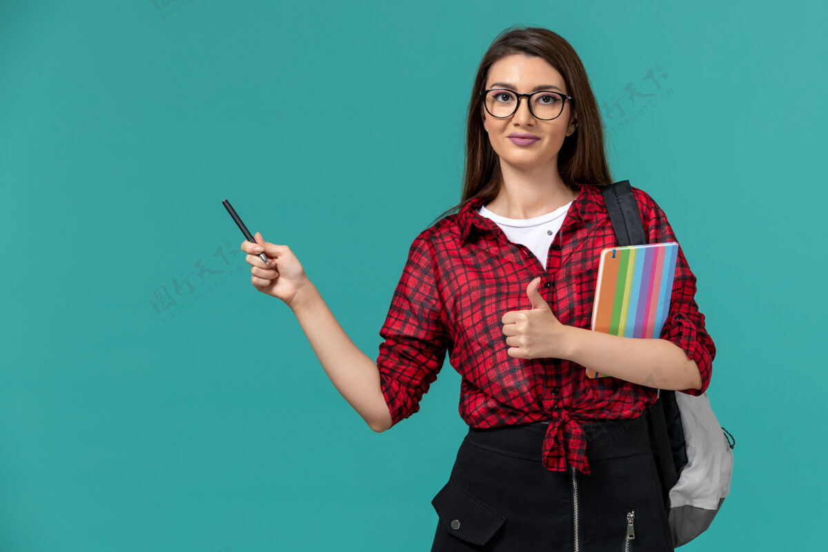 肖像女学生背着书包拿着文案和笔在蓝色墙上的正视图学生成人微笑