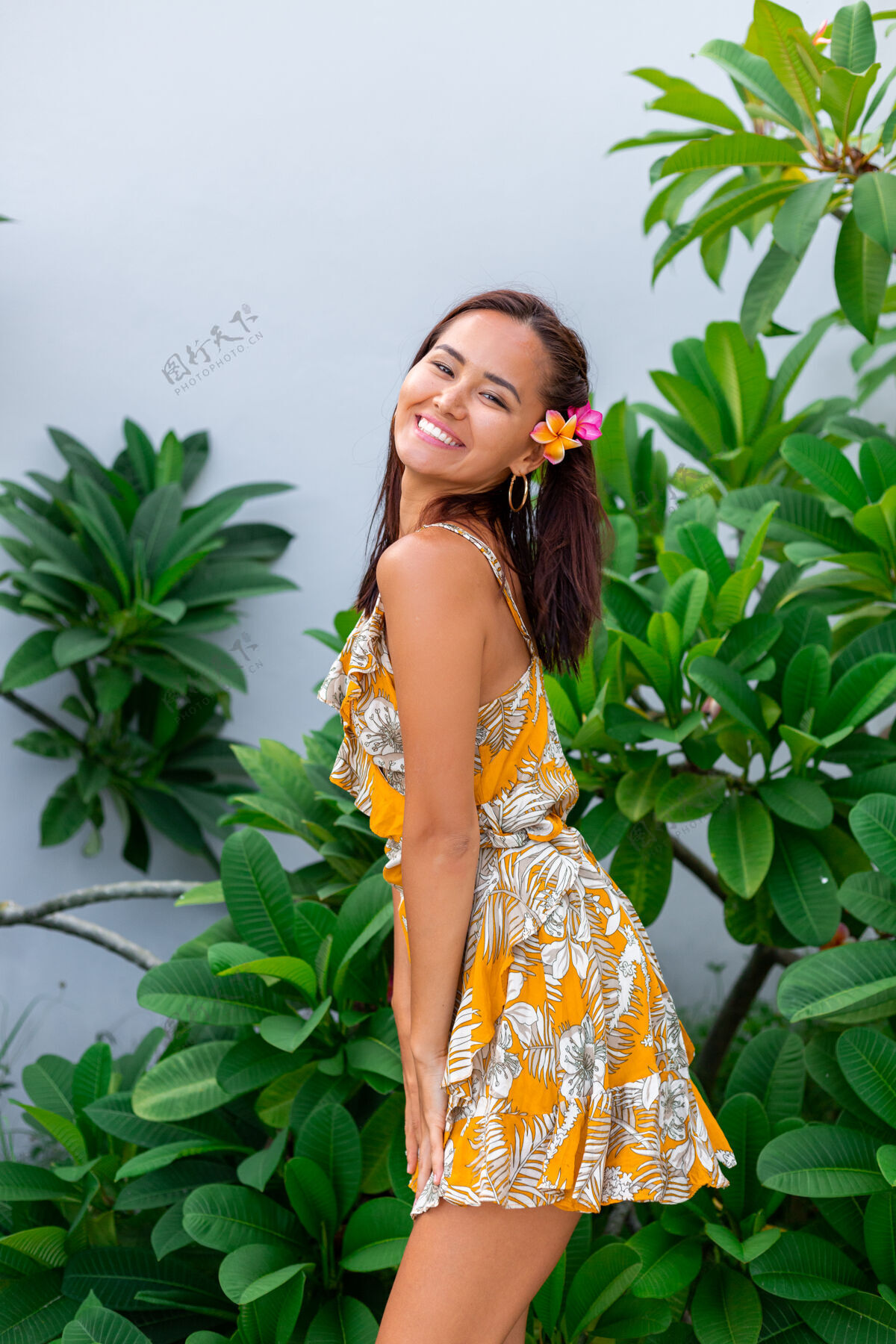 鸡蛋花身着黄色夏装的亚洲女人的肖像站在那里 头发上插着泰国花 戴着圆耳环美丽度假热带