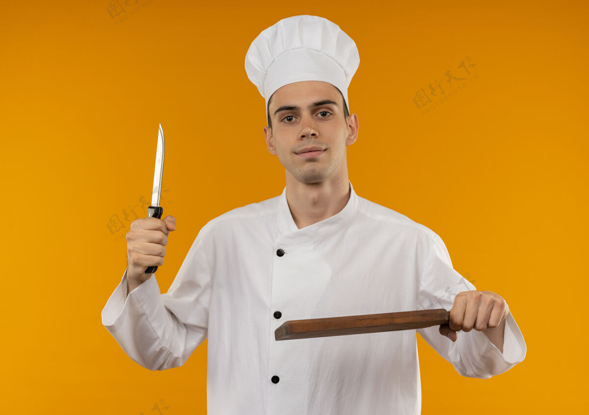 拿着高兴的年轻男酷穿着厨师制服拿着刀和砧板高兴厨师戴着