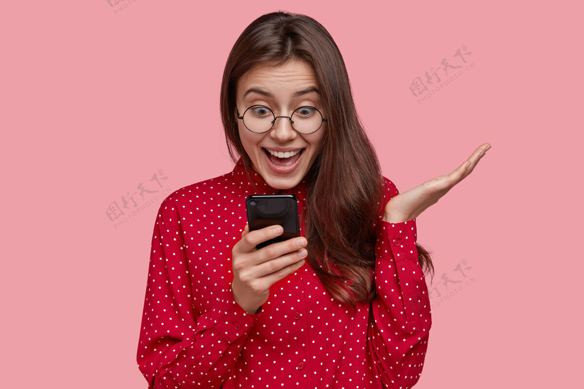 女性开心女人在手机上浏览网络 主动打手势 上网购物 穿红衫高兴设备波尔卡多