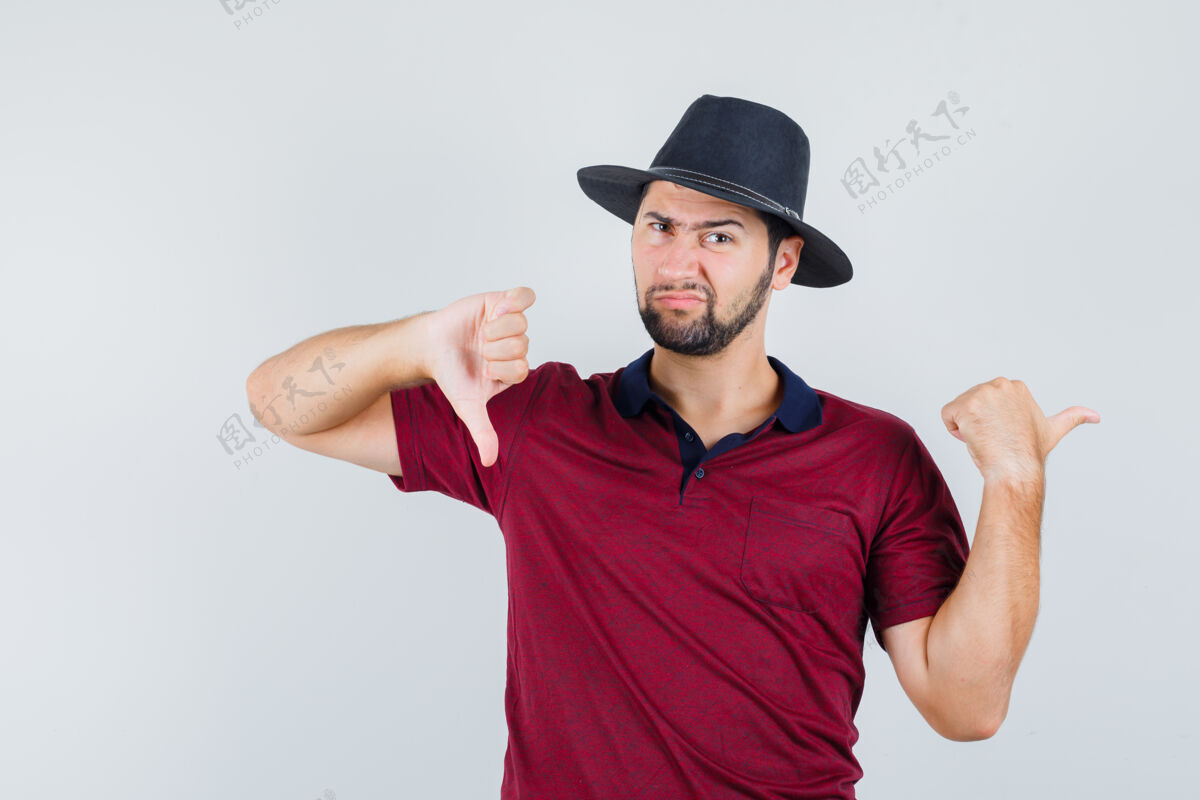 随意年轻男性一边指着一边 一边大拇指朝下穿t恤 戴着帽子 看上去很不满意 正面照指向时尚表情