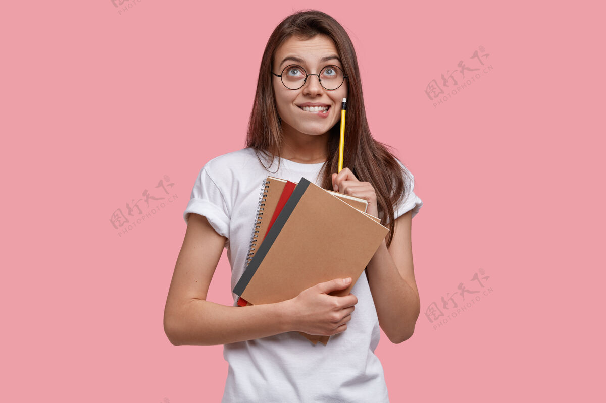教育高兴的欧洲小姐照片高高兴兴地向上看 拿着铅笔 课本 有梦幻般的表情 写下笔记想象满意散文