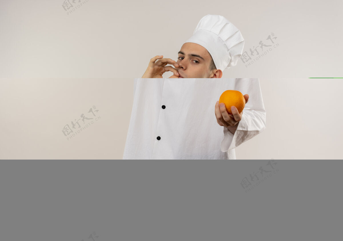 穿年轻的男厨师穿着厨师制服拿着橘子在隔离的白色墙壁上展示美味的手势 还有复制空间厨师厨师看