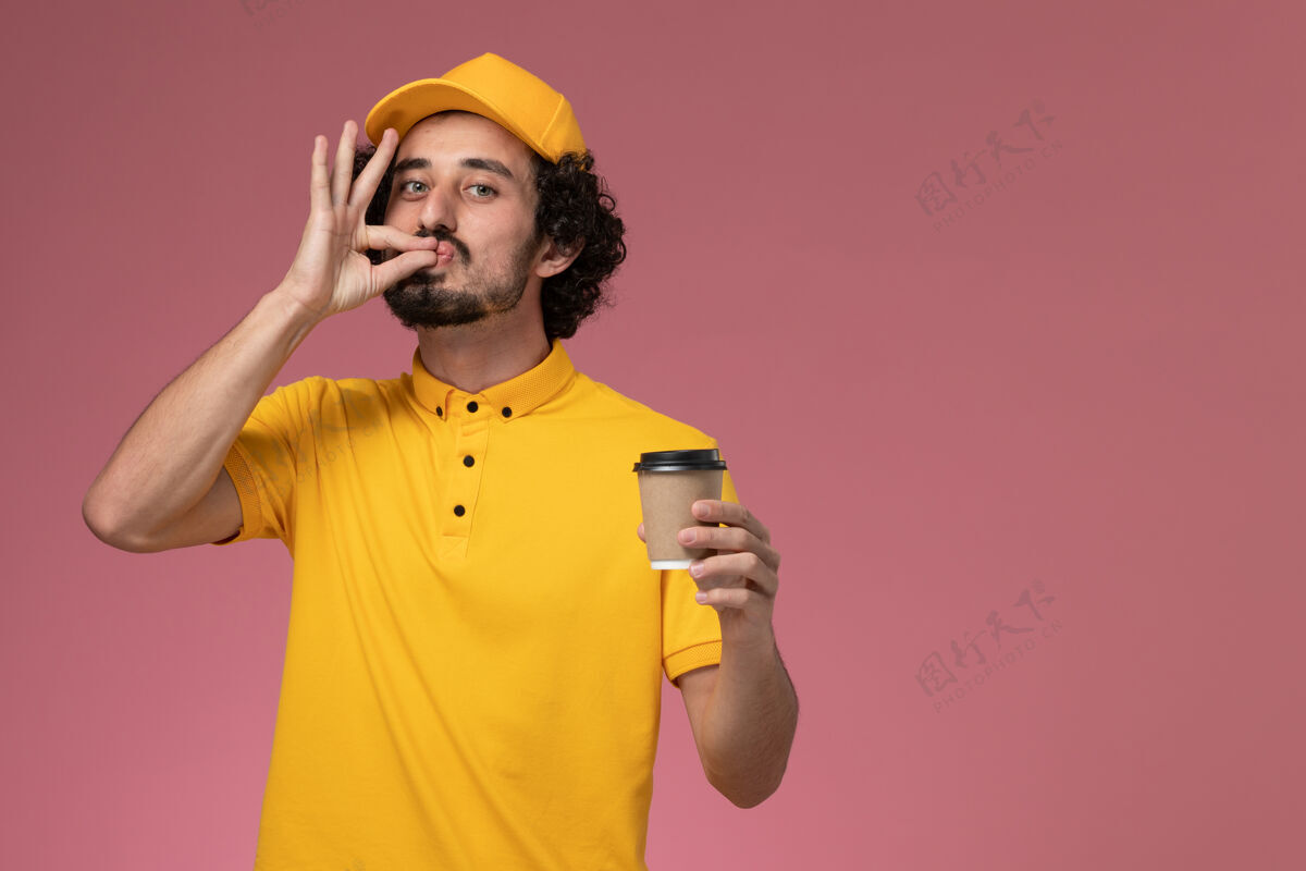 黄色正面图：身穿黄色制服 披风的男性快递员在粉色墙上拿着送货咖啡杯咖啡快递微笑