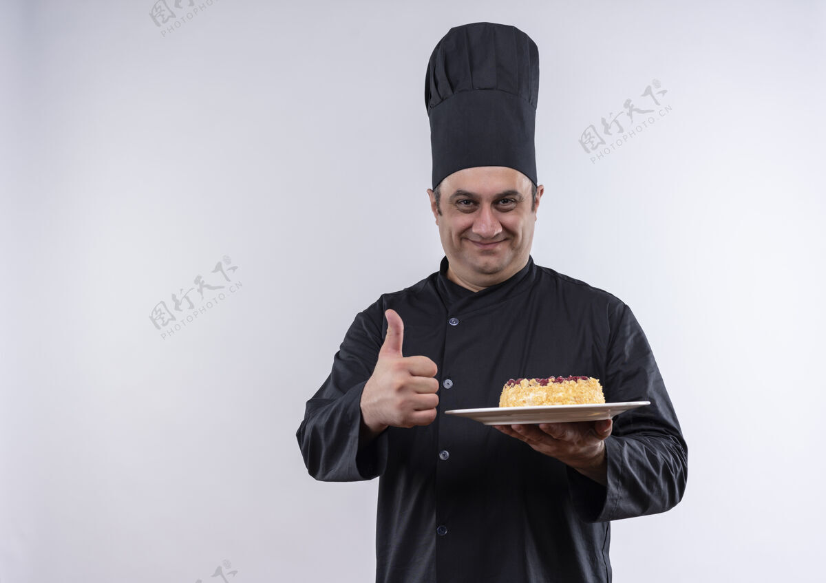制服一位身着厨师制服的中年男厨师拿着盘子上的蛋糕 大拇指竖立在隔离的白色墙壁上 上面留有复印空间厨师蛋糕男